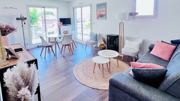 A modern living room with a grey sofa, a round coffee table, and a dining area with chairs and a table. - Arcachon: Bright apartment with a balcony, just 1 minute from the beach (Arcachon)