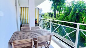 A balcony with a wooden table and chairs, a potted plant, and a view of greenery. - Arcachon: Bright apartment with a balcony, just 1 minute from the beach (Arcachon)