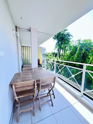 Ein Balkon mit Holztisch und -stühlen, einem Blumentopf und Blick ins Grüne.