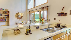 Eine Küche mit einem großen Fenster, einer Spüle und einer Arbeitsplatte mit Korb und Flaschen.