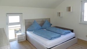 Un dormitorio con cama, mesita de noche, ventana y puerta.