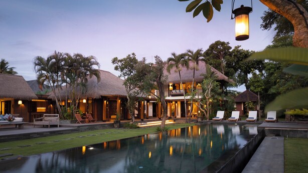 Un resort con edificios de techo de paja, una piscina y sillones de descanso.