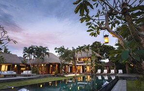 Een resort met rieten villa’s, een zwembad en ligbedden.