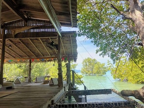 Een houten terras met rieten dak, met uitzicht op een wateroppervlak, omgeven door groen.