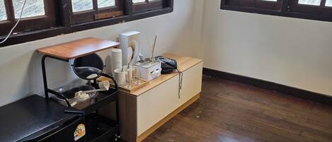 A room with a wooden floor, a desk with a computer, a fan, and a window with a view of greenery.
