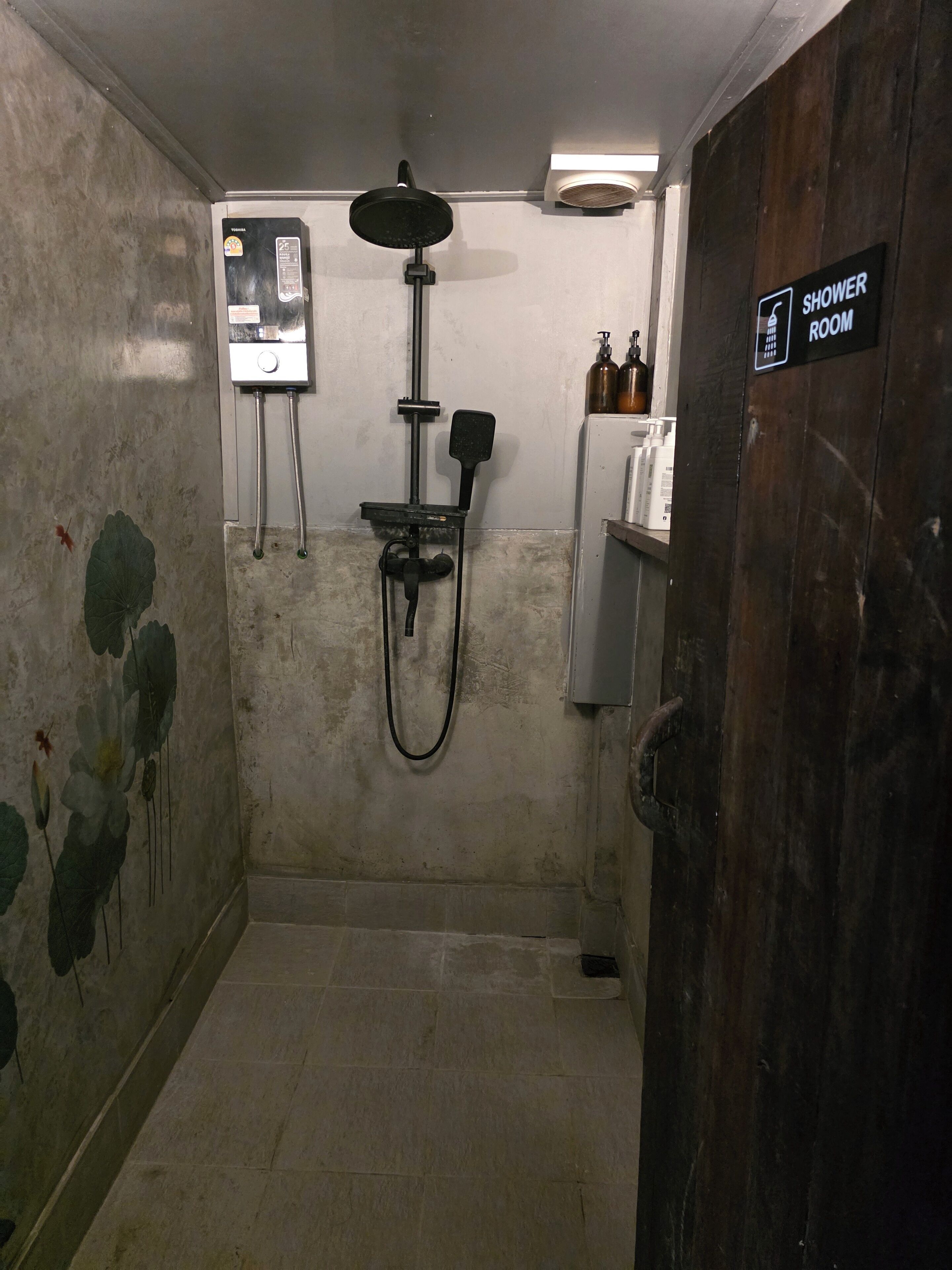 A shower room with a handheld showerhead, a wall-mounted faucet, and a sign indicating the room's purpose.