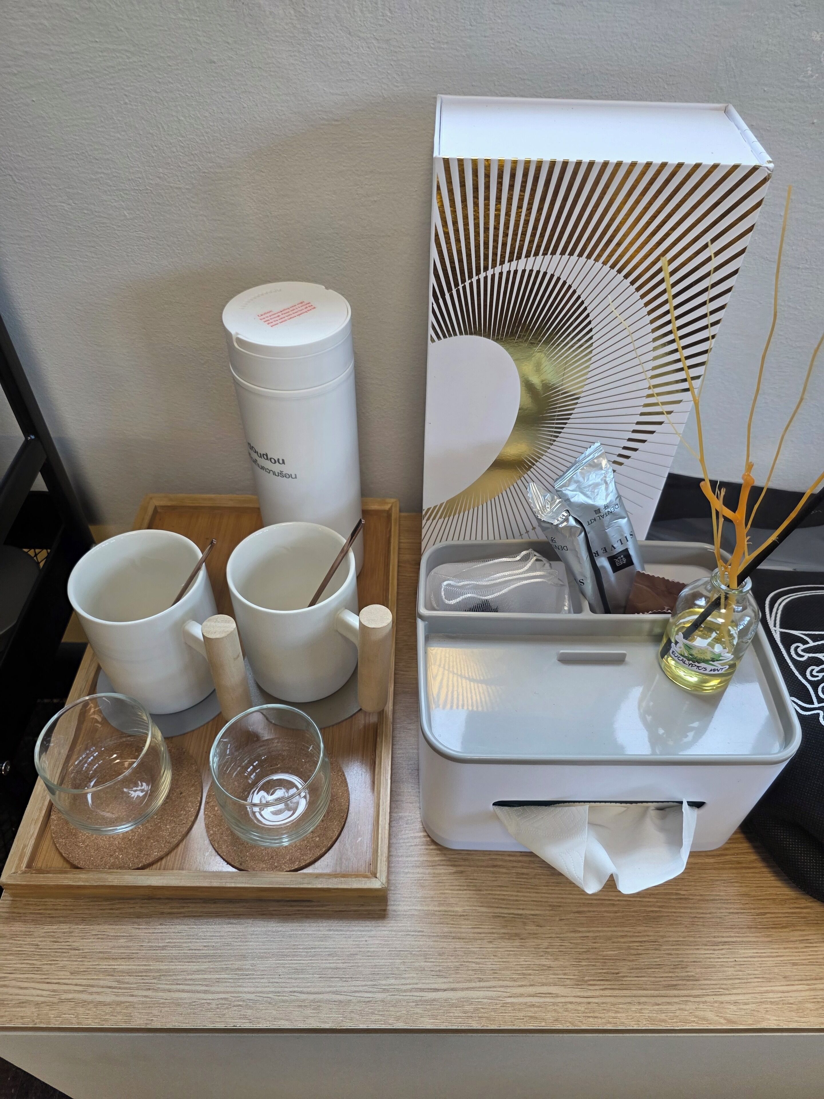 A neatly organized tray with white mugs, a wooden spoon, and a glass with a straw.