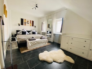 A bedroom with a bed, bedside tables, a mirror, a radiator, and a white fur rug.