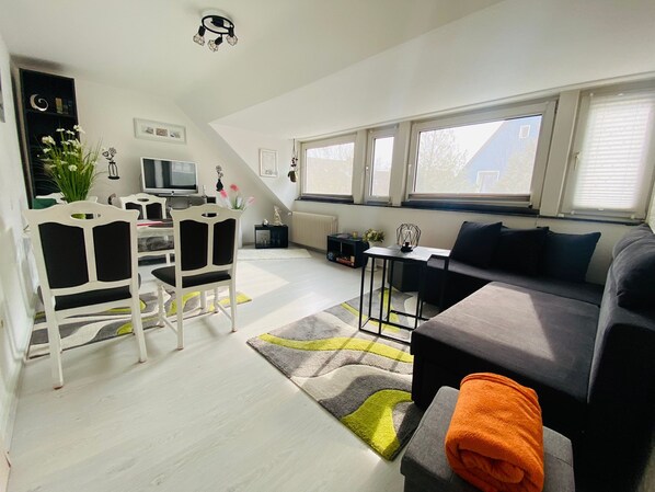 A modern living space with a dining area, a sofa, and a TV.