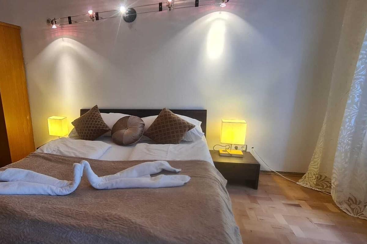 Una cama bien tendida con dos almohadas, un armario de madera y dos lámparas de noche.