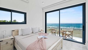 Un dormitorio con una cama grande, una mesita de noche y vistas a la playa a través de un ventanal amplio.