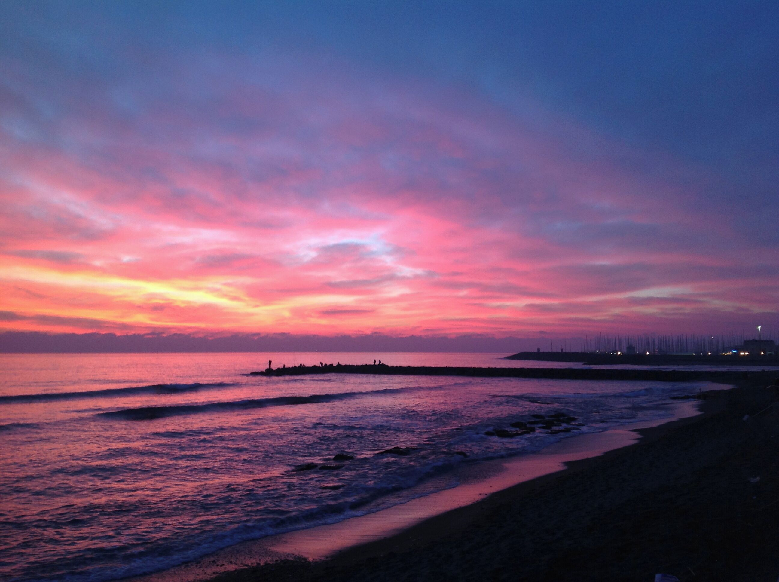 Une plage au coucher du soleil, avec une jetée qui s’avance dans l’eau.