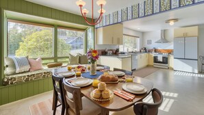 Un comedor con una mesa de madera dispuesta para el desayuno, un banco empotrado con cojines y vistas a la cocina.