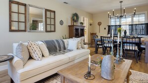 A living room with a sofa, coffee table, and dining area with chairs and a chandelier.