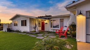 A two-story house with a well-maintained lawn, a red door, and a red chair outside.