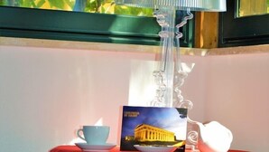 A table with a red and blue tablecloth, a clear glass lamp, a blue cup, a saucer, a book, and a white object on the table. - Exclusive Flats inside 4 Stars Resort (Laura)
