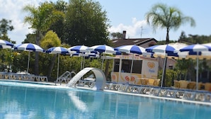 A swimming pool with blue and white umbrellas, a water slide, and a building with 'Algida' branding. - Exclusive Flats inside 4 Stars Resort (Laura)