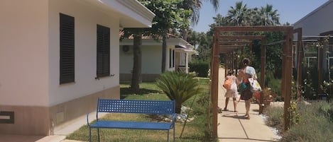 A pathway leading to a building with a blue bench and a wooden pergola.