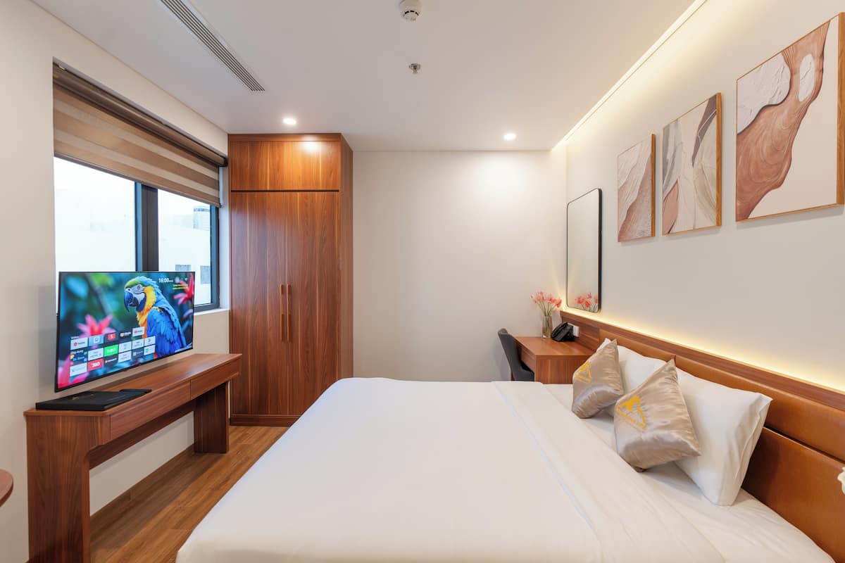 Une chambre d’hôtel moderne avec un grand lit, un téléviseur posé sur un meuble en bois, une armoire et des œuvres d’art accrochées au mur.