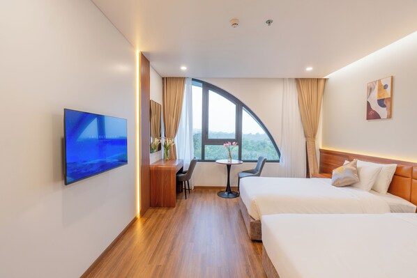Une chambre d’hôtel moderne dotée d’une fenêtre incurvée, d’un bureau avec une chaise, d’une télévision et de deux lits.