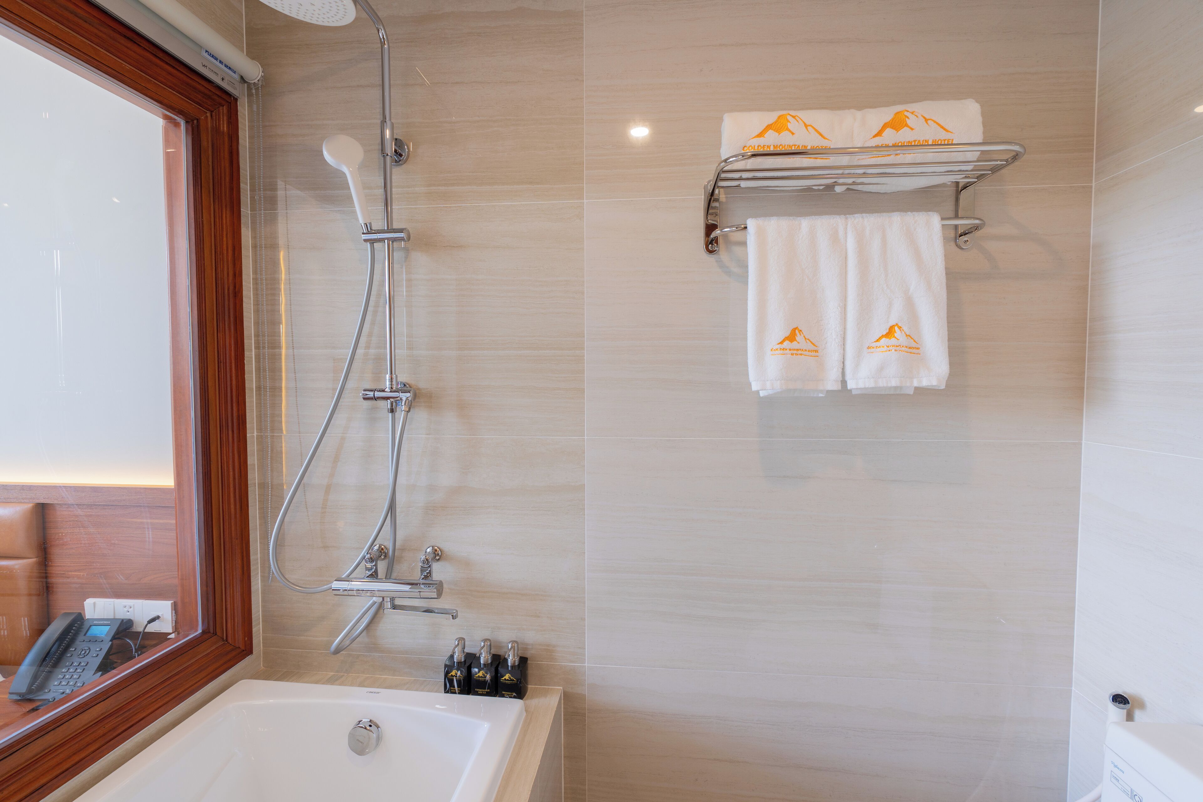 Een badkamer met een bad, een douche met handdouche, een handdoekrek met twee handdoeken en een raam met houten kader.