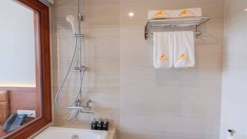 Een badkamer met een bad, een douche met handdouche, een handdoekrek met twee handdoeken en een raam met houten kader.