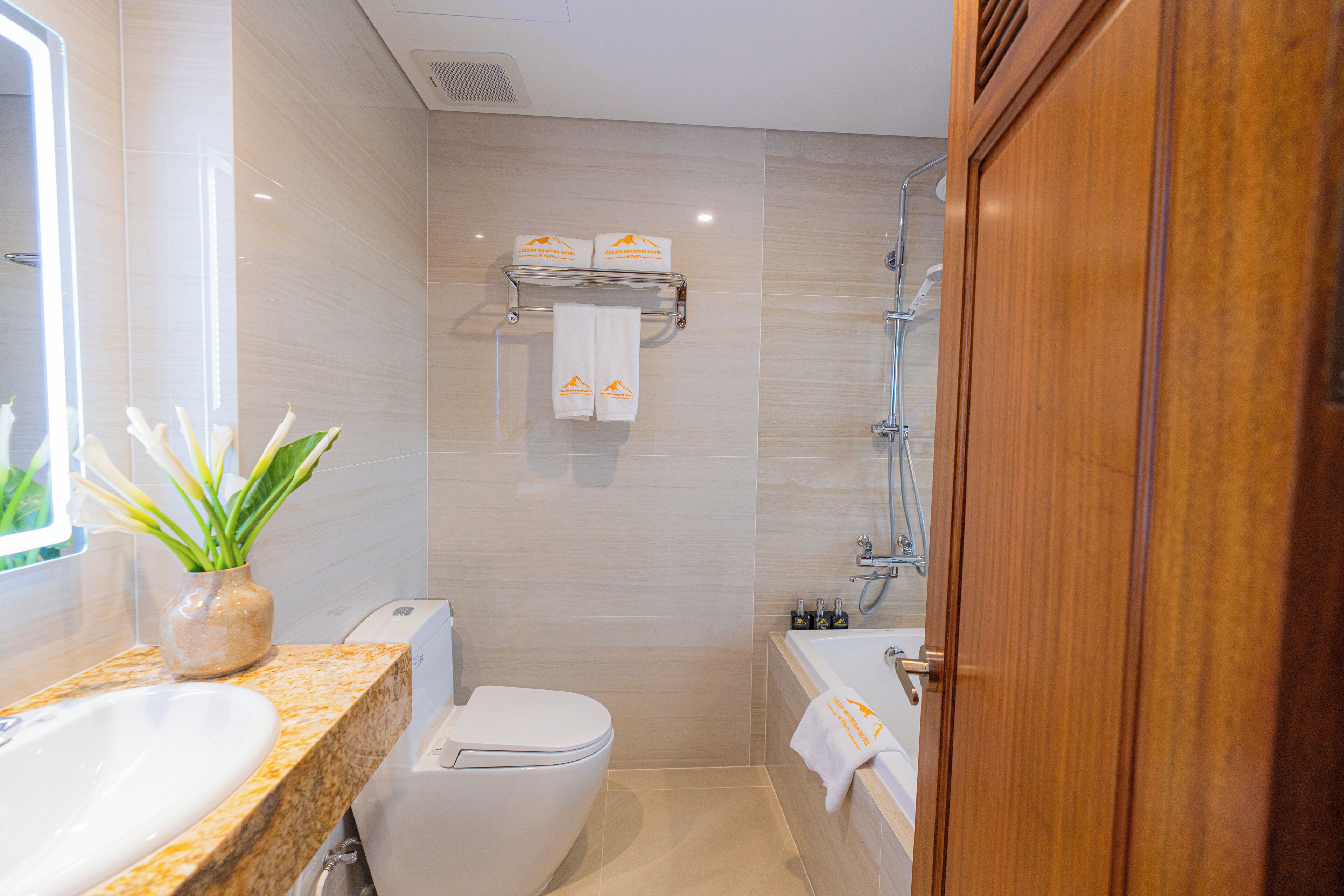 A modern bathroom with a sink, toilet, and bathtub. There are towels hanging on a rack, and a plant on the counter.