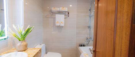 A modern bathroom with a sink, toilet, and bathtub. There are towels hanging on a rack, and a plant on the counter.