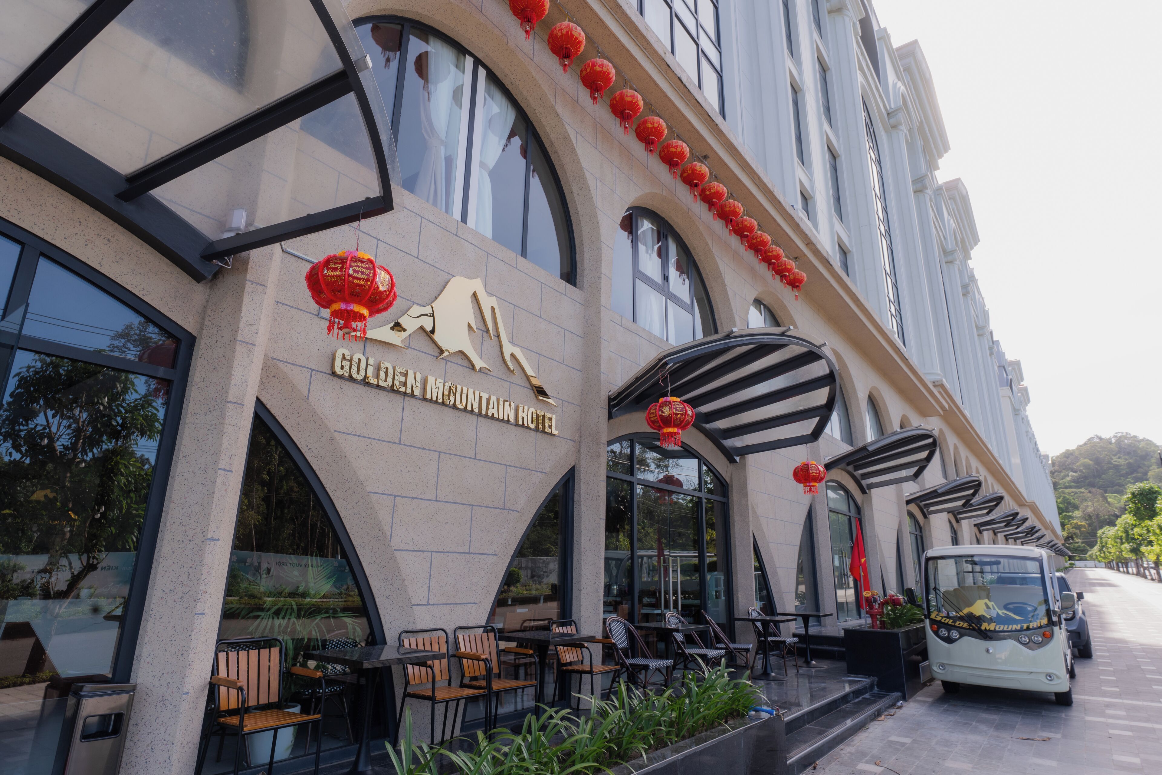 The exterior of the Golden Mountain Hotel with outdoor seating and a parked bus.