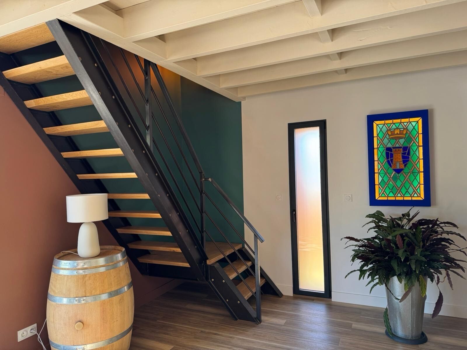 Un interior moderno con una escalera de madera, una planta en maceta y un ventanal con vitrales.
