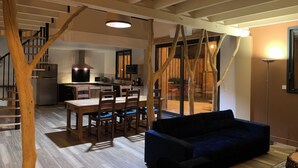A modern kitchen with a built-in stove, microwave, and refrigerator. There is a dining area with a wooden table and chairs. A blue sofa is in the foreground. - Gîtes Barns de la Truffière: Loft Côté Cuvier (Monbazillac)