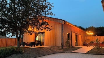 Un bâtiment moderne doté d’une façade incurvée, d’un espace extérieur couvert aménagé en coin salon et d’un chemin de gravier menant à l’entrée.