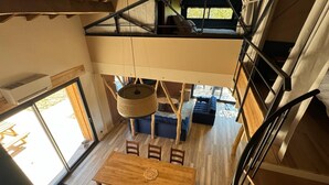 A spacious loft-style room with a high ceiling, a dining area with a wooden table and chairs, a cozy seating area with blue sofas, and a staircase leading to an upper level. - Gîtes Barns de la Truffière: Loft Côté Cuvier (Monbazillac)