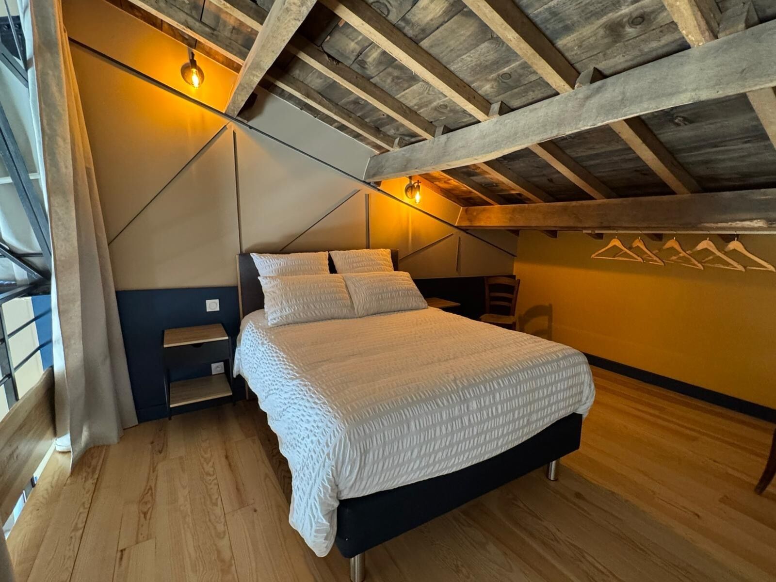 Een slaapkamer met een houten plafond, een bed met wit beddengoed, een nachtkastje en een wandplank.