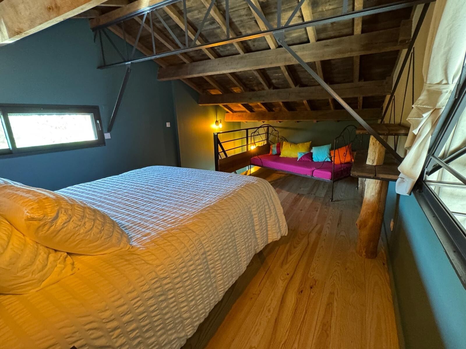 A bedroom with a bed, a hanging chair, and a staircase.
