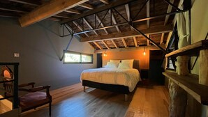 A bedroom with a wooden ceiling, a bed, a chair, and a window. - Gîtes Barns de la Truffière : Loft Coté Grange (Monbazillac)