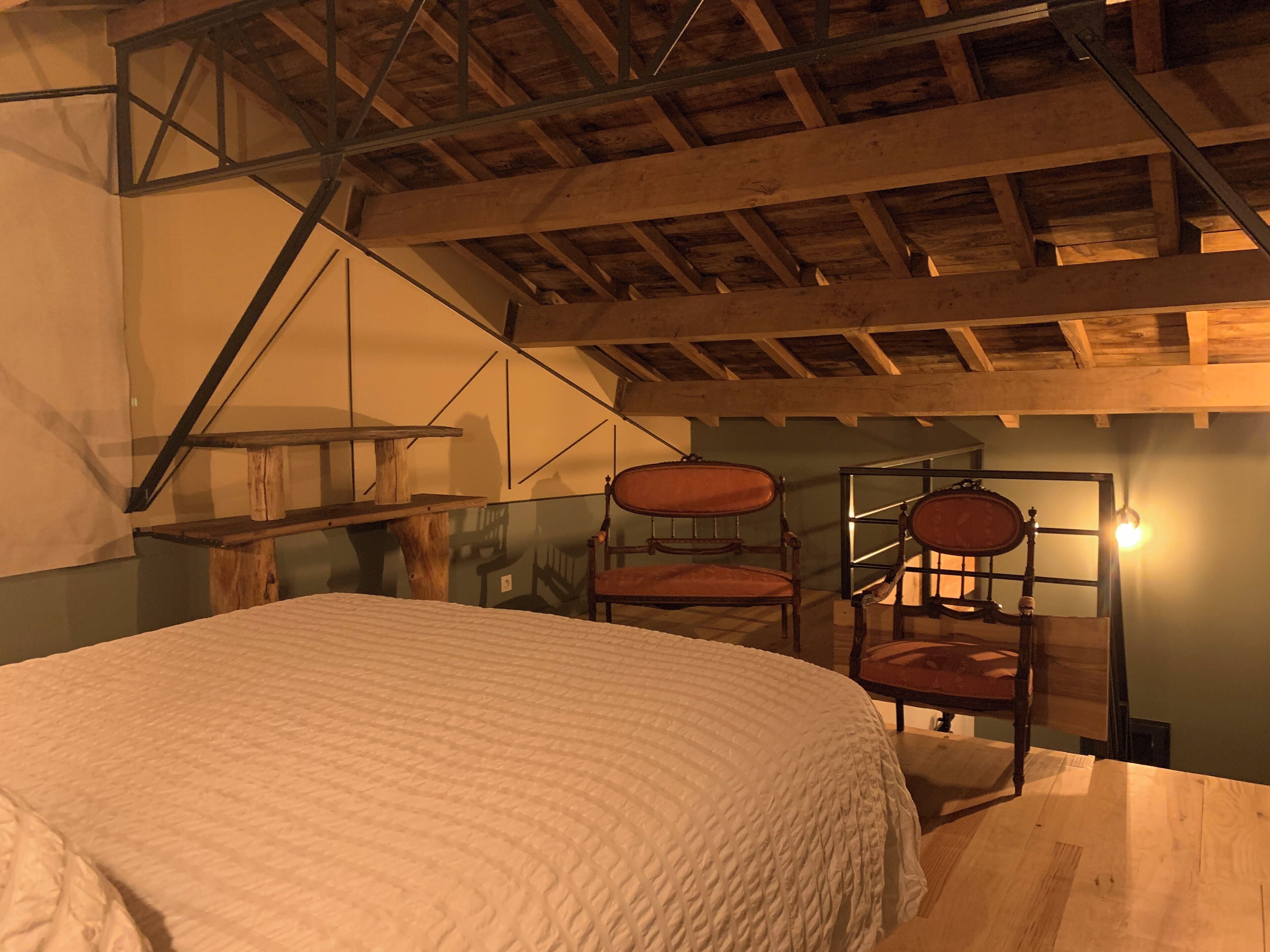 Ein Zimmer mit einem Bett, zwei Stühlen, einem Holztisch und einer schrägen Decke mit freiliegenden Balken.