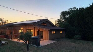 A modern house with a sloped roof, solar panels, and a small front yard with a tree and a bench. - Gîtes Barns de la Truffière : Loft Coté Grange (Monbazillac)
