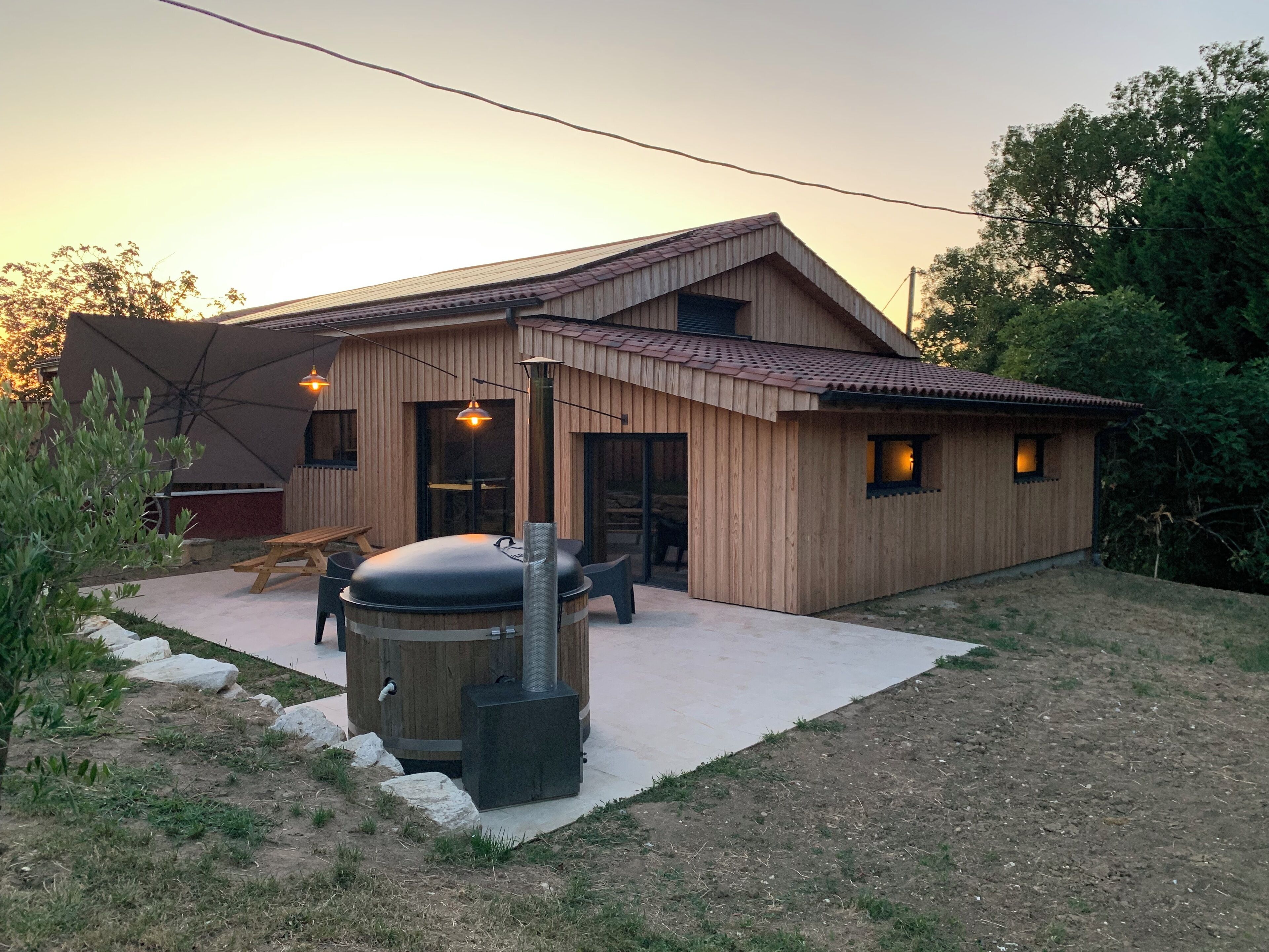 Une maison en bois dotée d’un patio, d’un barbecue et d’un coin repas.