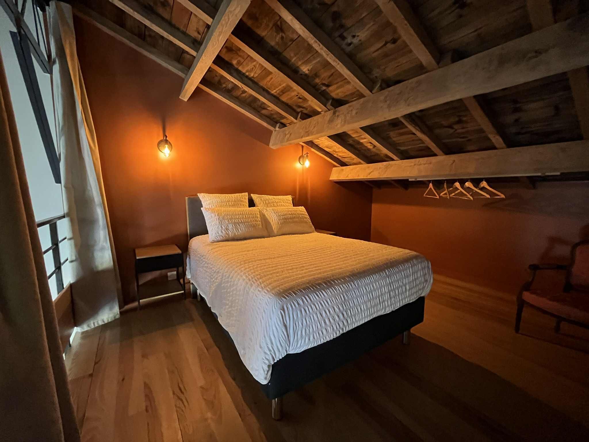Une chambre avec un plafond en bois, un lit avec une literie blanche et deux appliques murales.