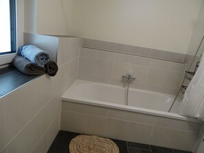 Ein Badezimmer mit einer Badewanne, einem Fenster und Handtüchern auf einem Regal.