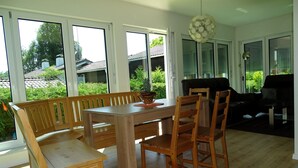 A dining area with a wooden table and chairs, large windows, and a view of greenery outside. - Sunny house with 2 residential units, large garden and sun terrace (Postmünster)