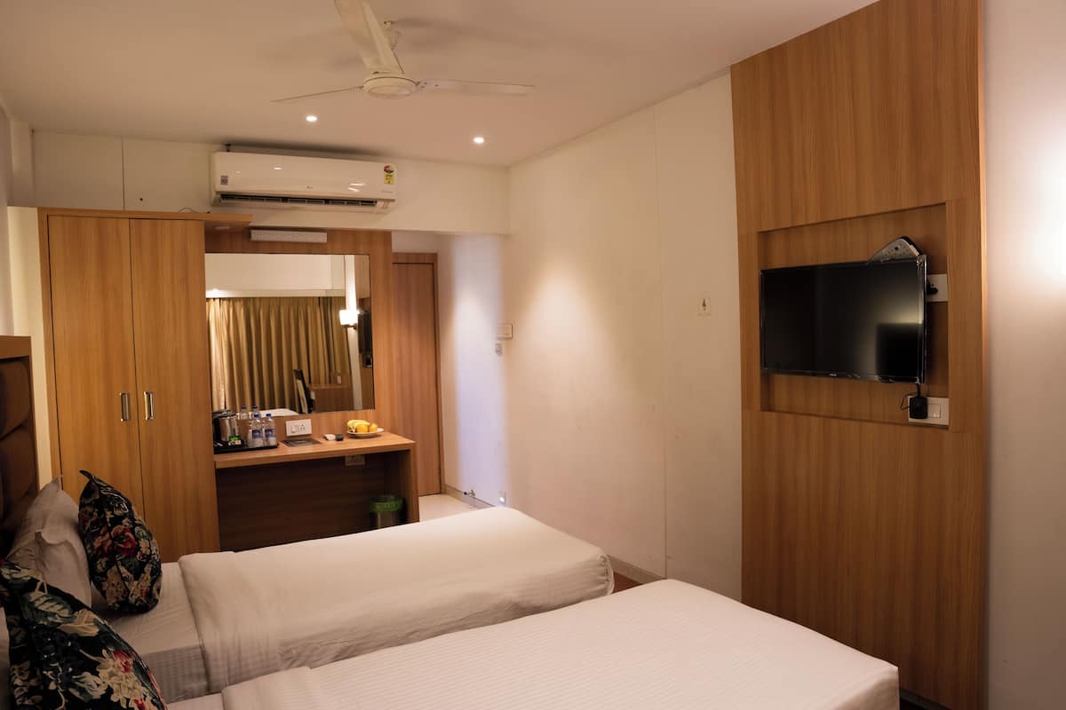 A hotel room with two beds, a wooden wardrobe, a desk with a mirror, and a mounted TV.