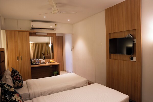A hotel room with two beds, a wooden wardrobe, a desk with a mirror, and a mounted TV.