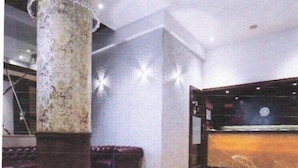Un hall d’entrée avec un comptoir de réception en marbre, une grande colonne et un espace détente aux couleurs violettes.