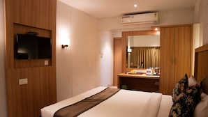 Une chambre d’hôtel comprenant un lit, un téléviseur fixé au mur, une armoire en bois, un miroir et une salle de bain avec un lavabo et des serviettes.