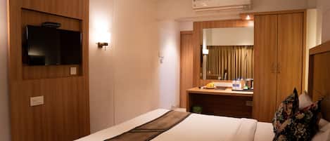 A hotel room with a bed, a television, a mirror, a desk with toiletries, and an air conditioning unit.