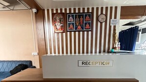 A reception desk with a sign labeled "RECEPTION," a clock, and a wall-mounted photo collage. - Hotel Akshar Palace (Vadodara)
