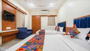 A hotel room with two beds, a sofa, a TV, and a wooden wall unit. - Hotel Akshar Palace (Vadodara)