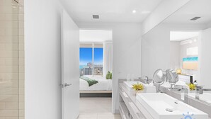 A modern bathroom with a large mirror, two sinks, and a view of a cityscape through an open door. - Wrap Around Balcony + Pool + Steps to the Beach (Hollywood)